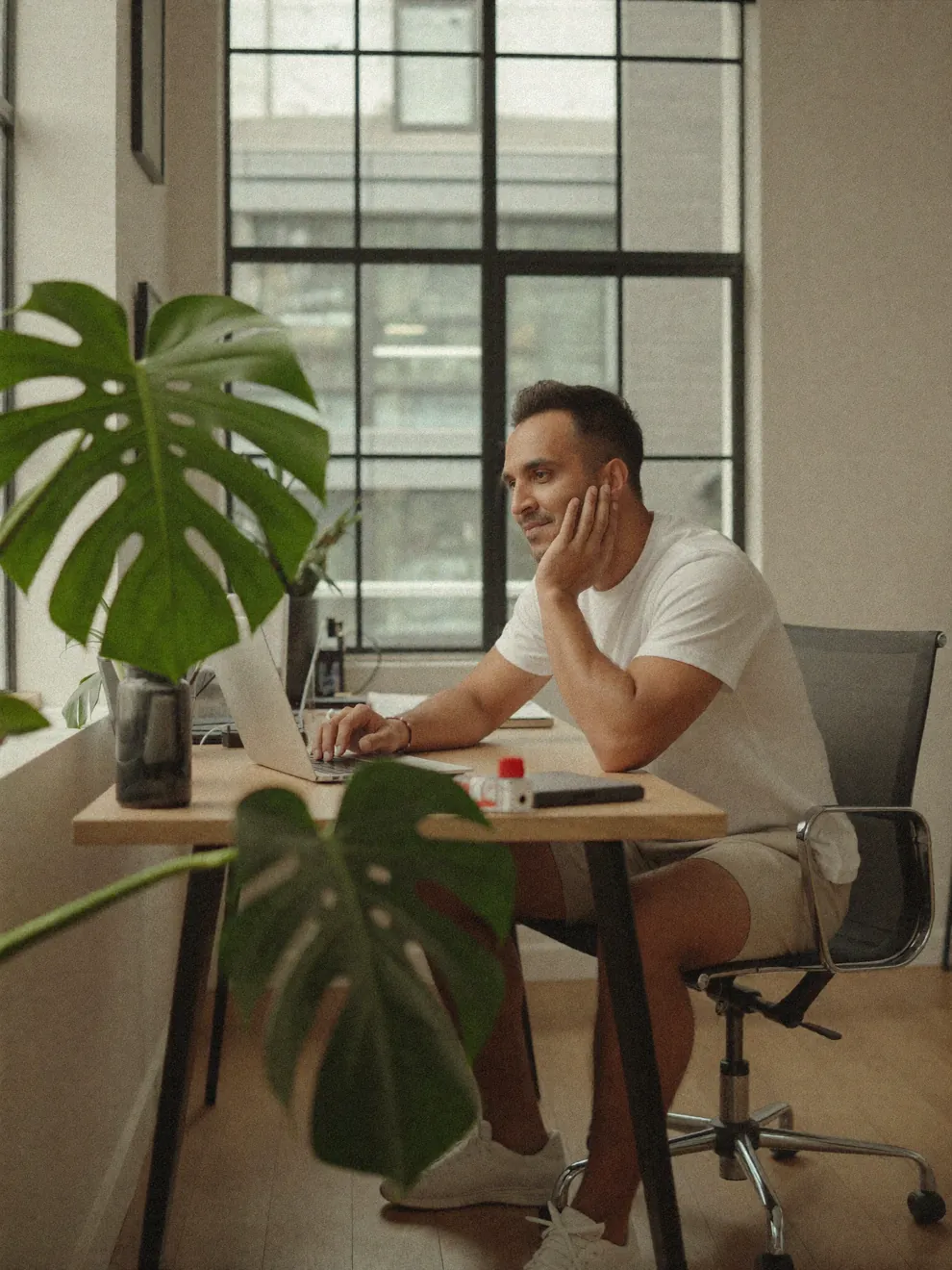 Rahim, Squarespace designer and founder of SQSP, working on a laptop at his studio desk by a tall window