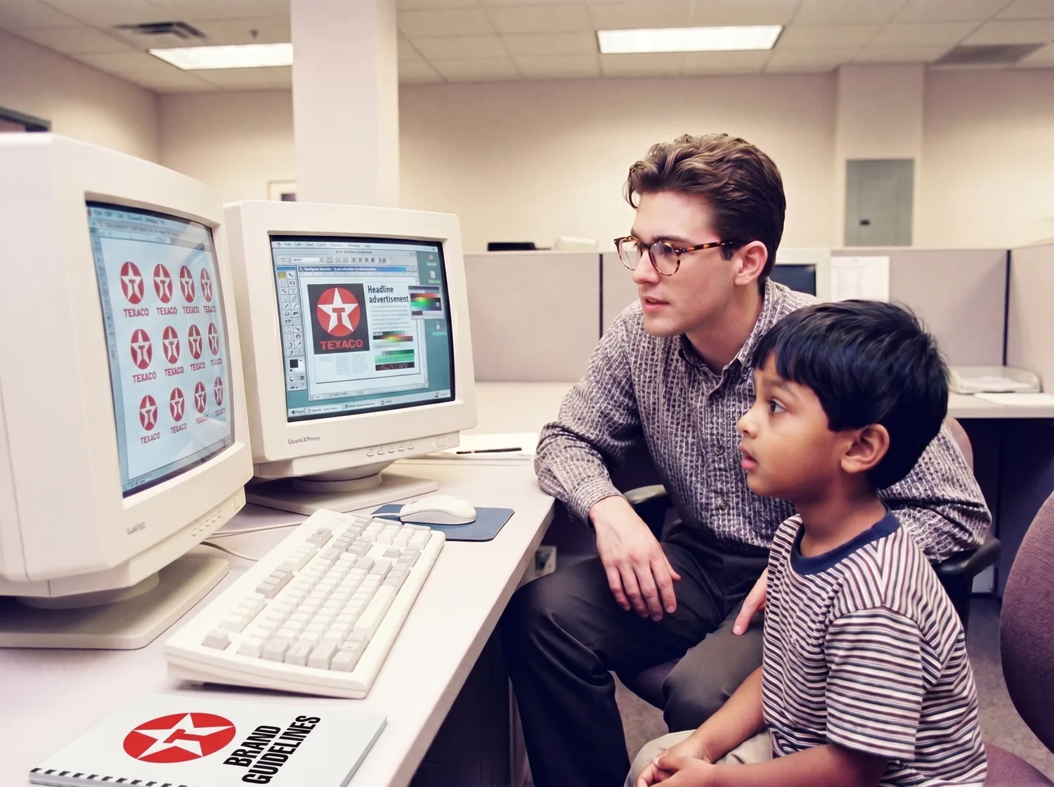 A young Rahim watching a designer work on Texaco brand layouts at two screens in a marketing studio — the moment he knew what he wanted to do