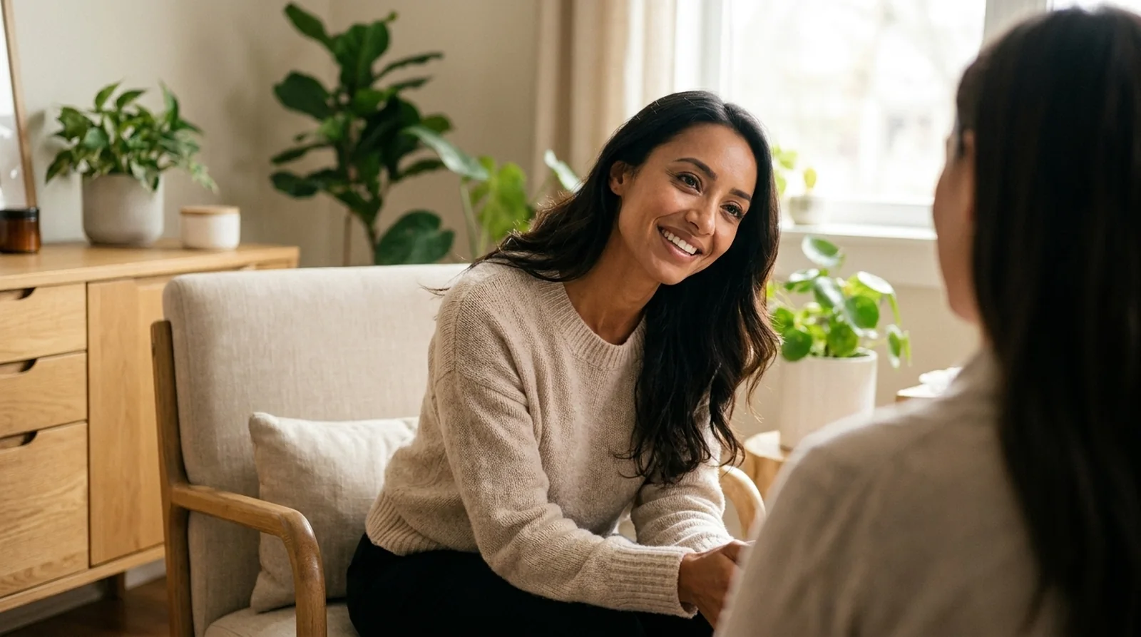 A warm therapist in a calm, attentive one-to-one conversation with a client in a serene sunlit therapy room